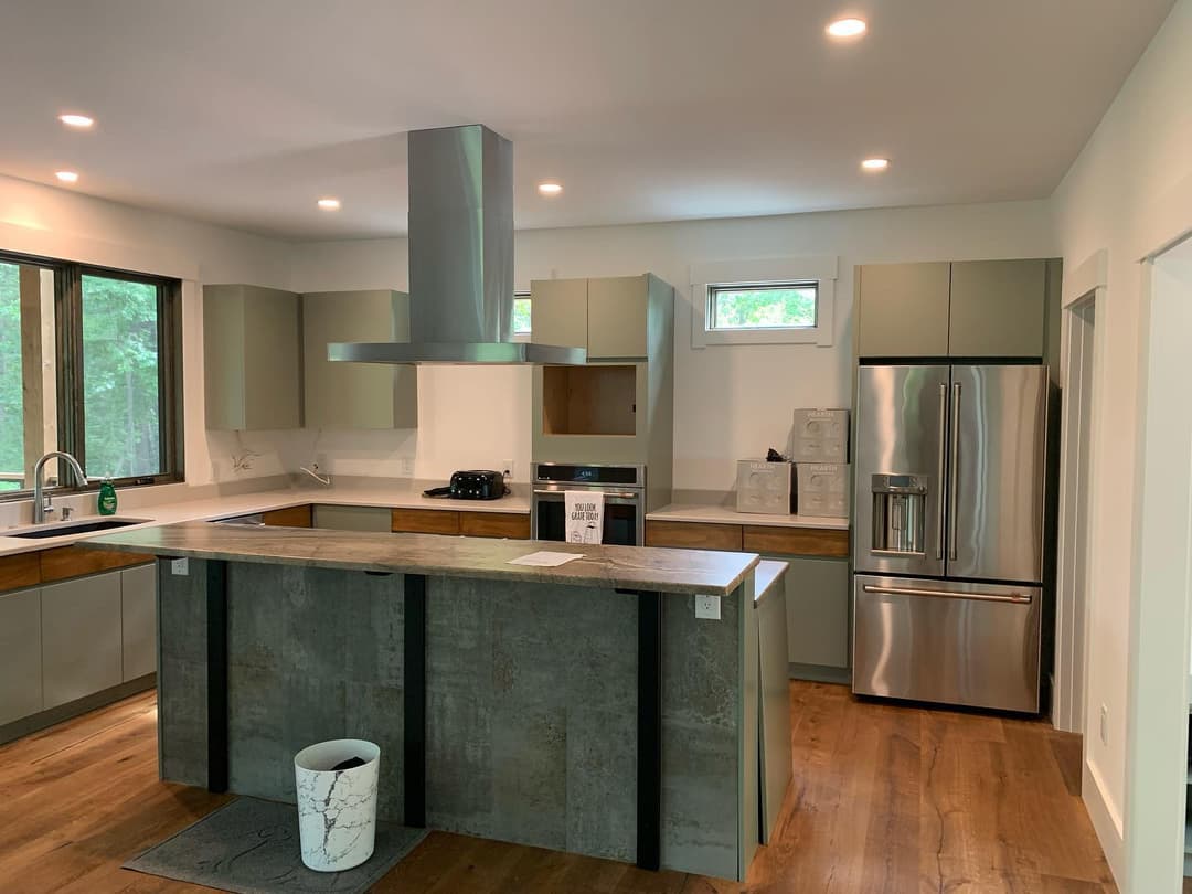 Modern kitchen with stainless steel appliances, concrete island, and natural light from windows.