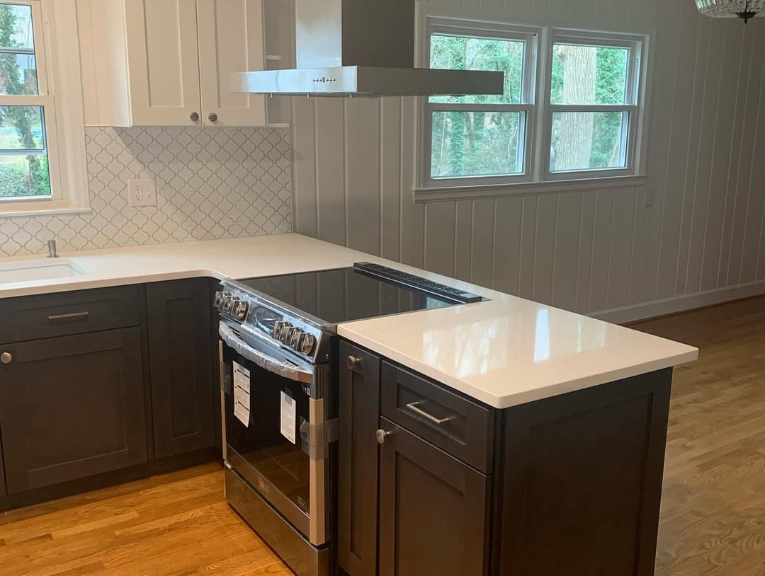 Modern kitchen with dark cabinetry, stainless steel stove, and white quartz countertops.