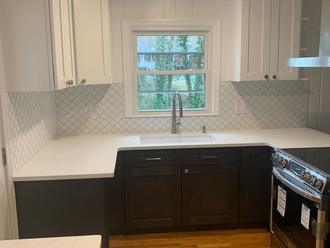 Modern kitchen with dark cabinets, white countertops, and a tiled backsplash, featuring a sink and window.