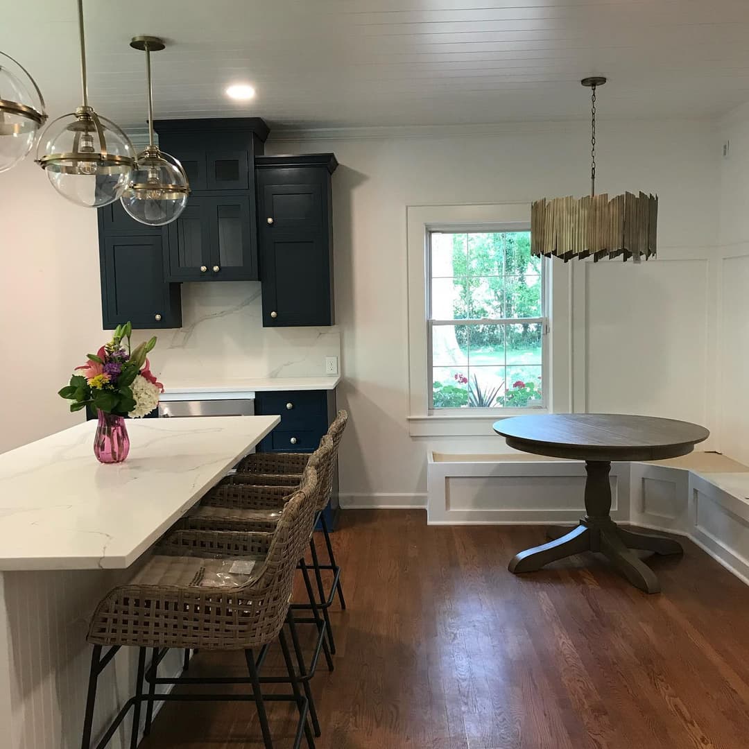 Modern kitchen with navy cabinets, marble countertop, and stylish dining area featuring floral decor.