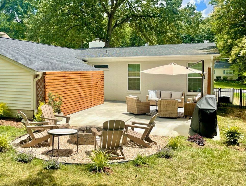 Cozy backyard patio with seating, umbrella, and fire pit surrounded by greenery.