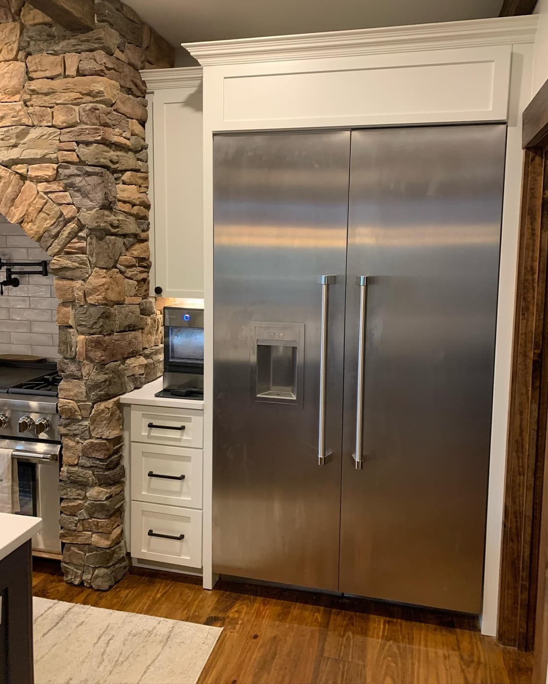 Modern kitchen featuring a stainless steel refrigerator and stone accent wall.