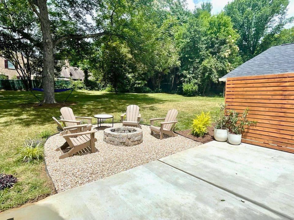 Cozy backyard seating area with four chairs around a stone fire pit and lush greenery.