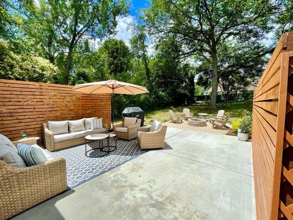 Cozy outdoor patio featuring woven furniture, umbrella, and lush greenery in a sunny setting.