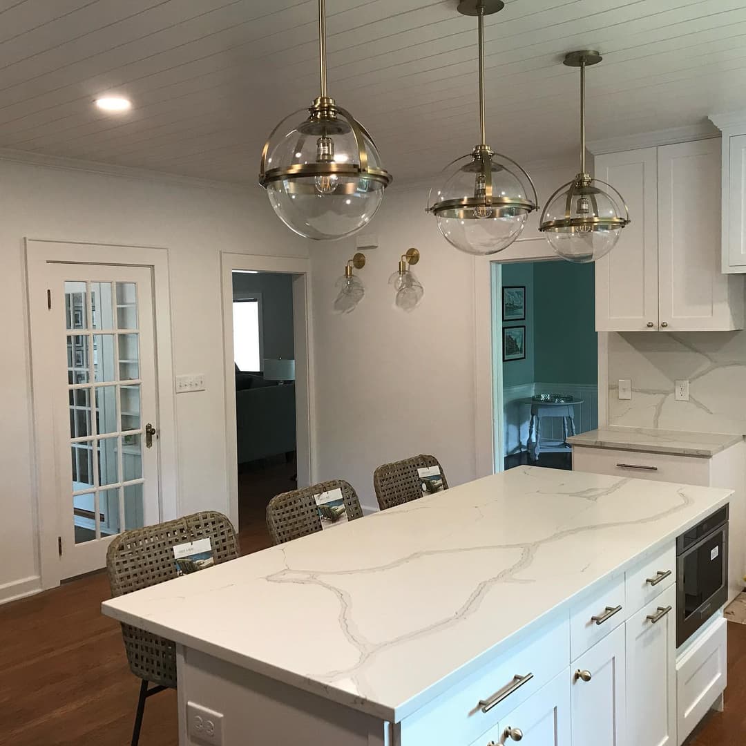 Modern kitchen featuring a white marble countertop, brass pendant lights, and stylish seating.