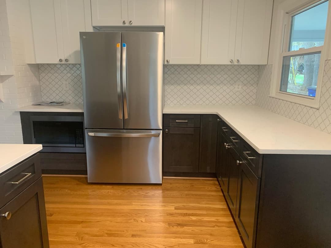 Modern kitchen featuring a stainless steel refrigerator, dark cabinetry, and white countertops.