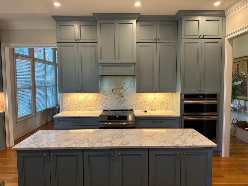 Modern kitchen design featuring gray cabinets, marble countertops, and stainless steel appliances.