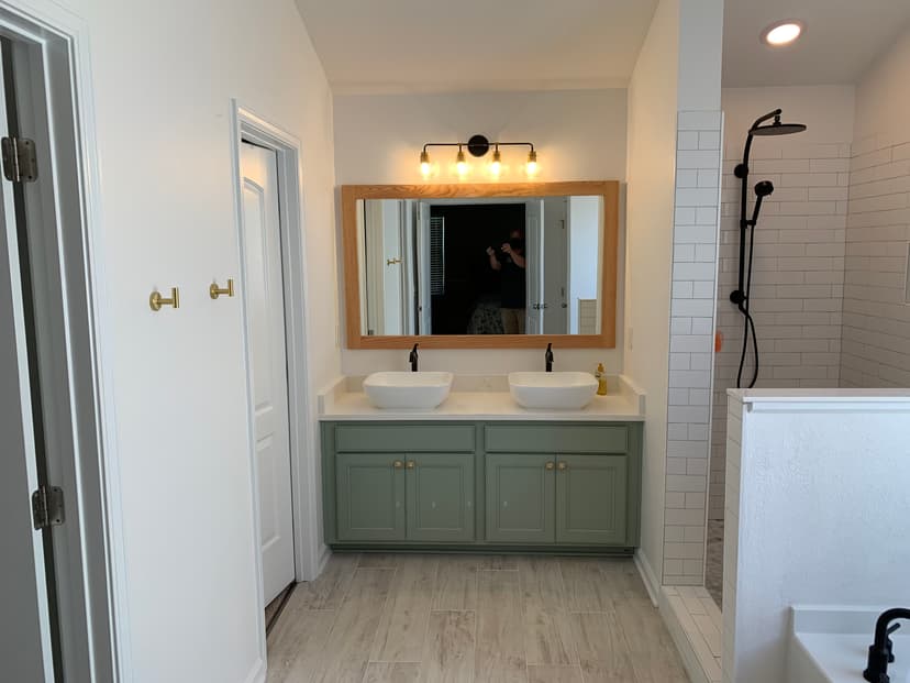 Modern bathroom with double sinks, green cabinetry, large mirror, and stylish shower area.