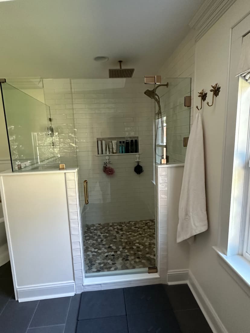 Modern glass shower with marble floor, white tiles, and stylish fixtures in a spacious bathroom.