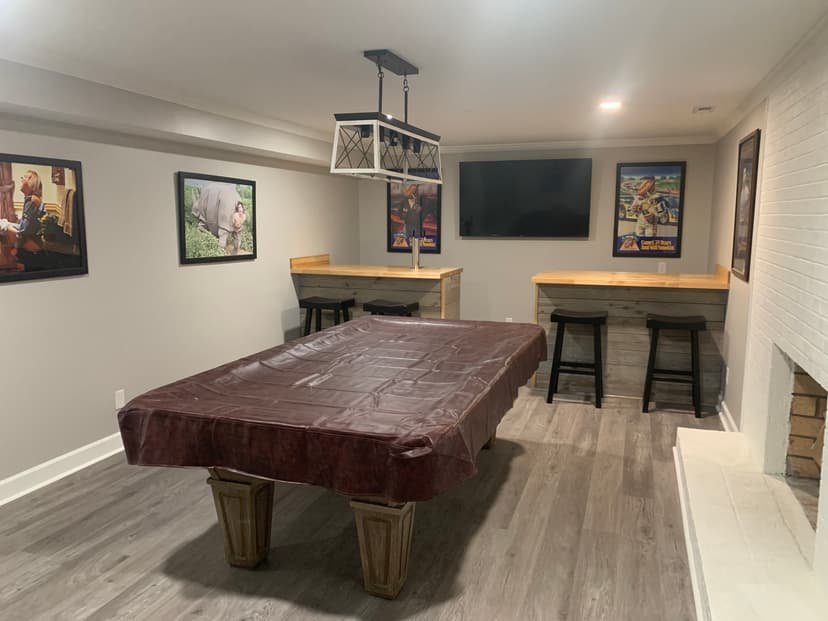 Modern basement game room with billiard table, bar seating, and movie posters on walls.