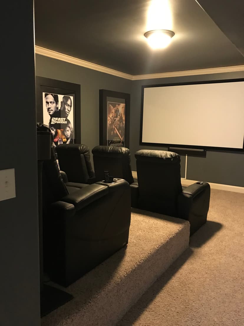 Home theater setup featuring leather recliners, large screen, and movie posters on the wall.