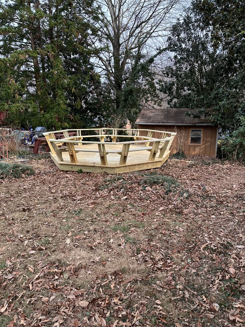 Wooden boat frame on a lawn surrounded by autumn leaves and a shed in the background.