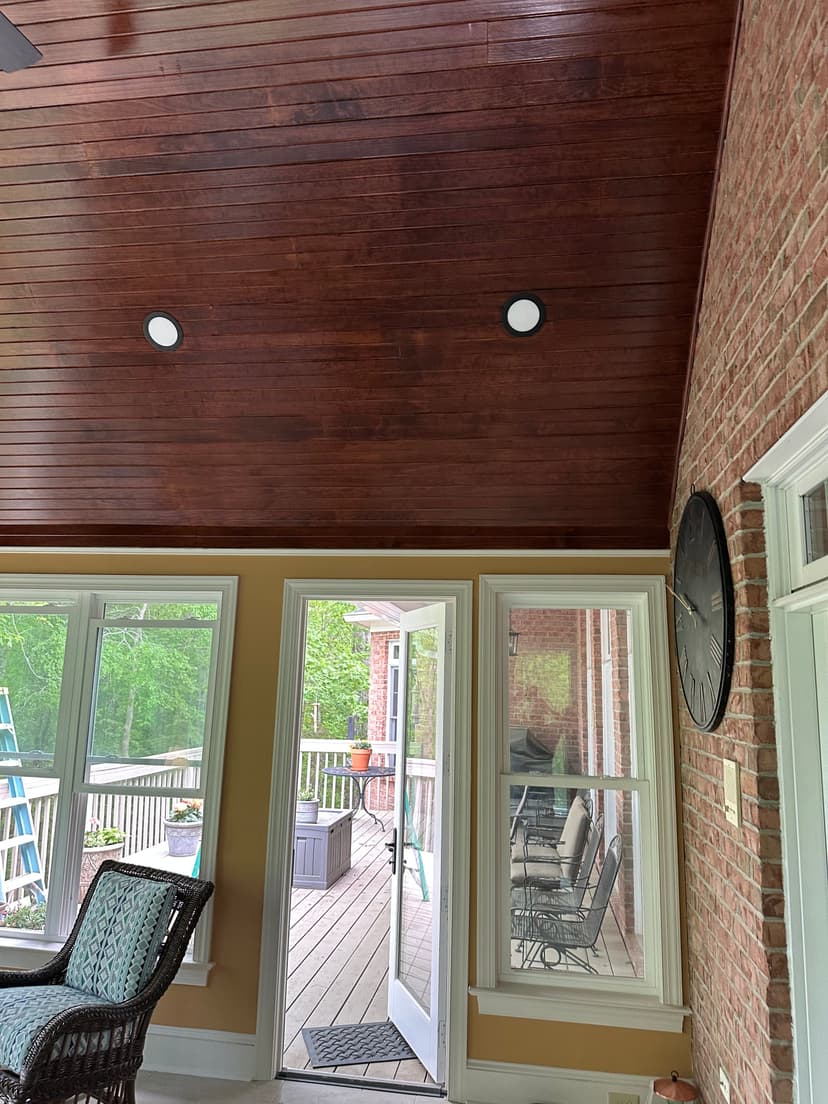 Interior of a sunroom with wooden ceiling, recessed lighting, and large windows.