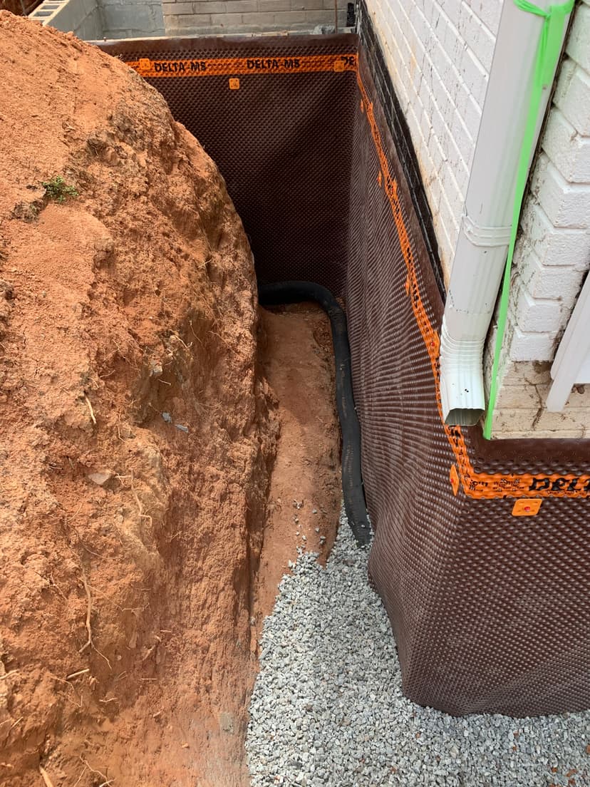 Drainage system installation beside home with gravel and excavation, ensuring proper water flow.