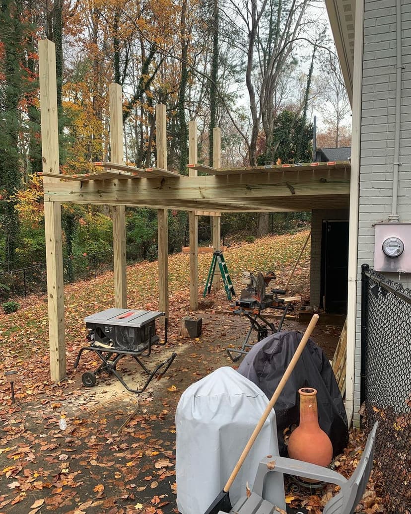 Under-construction wooden deck with support beams, autumn leaves scattered on the ground.