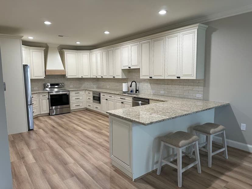 Modern kitchen with white cabinetry, granite countertops, stainless steel appliances, and hardwood flooring.