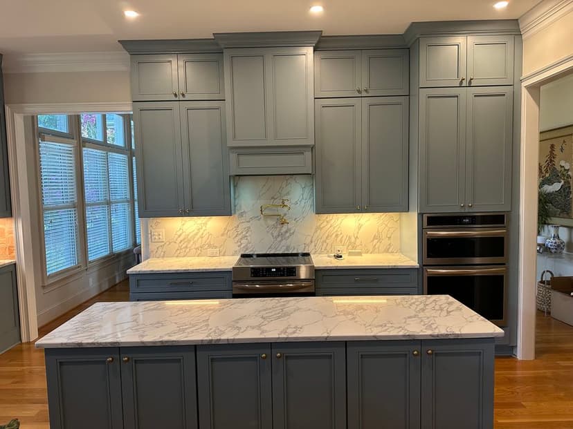 Modern kitchen with blue cabinetry, marble countertops, and stainless steel appliances.