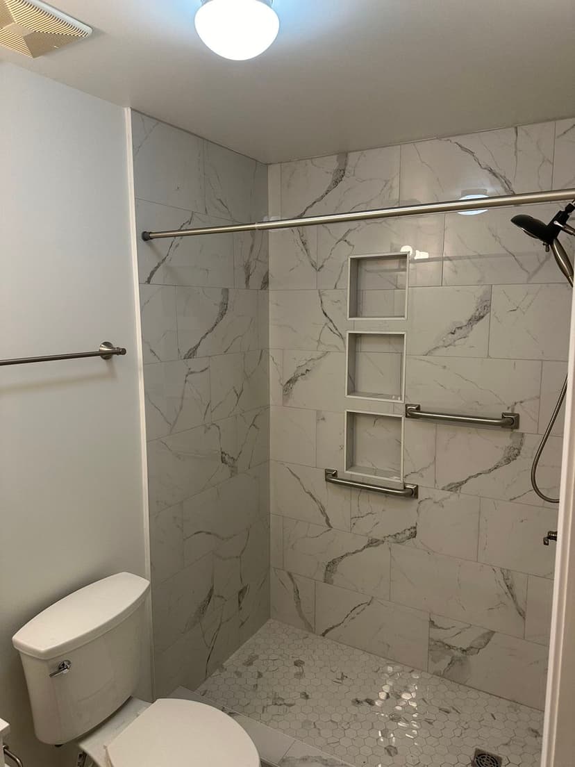 Modern bathroom with marble tile shower, grab bars, and hexagon tile flooring.