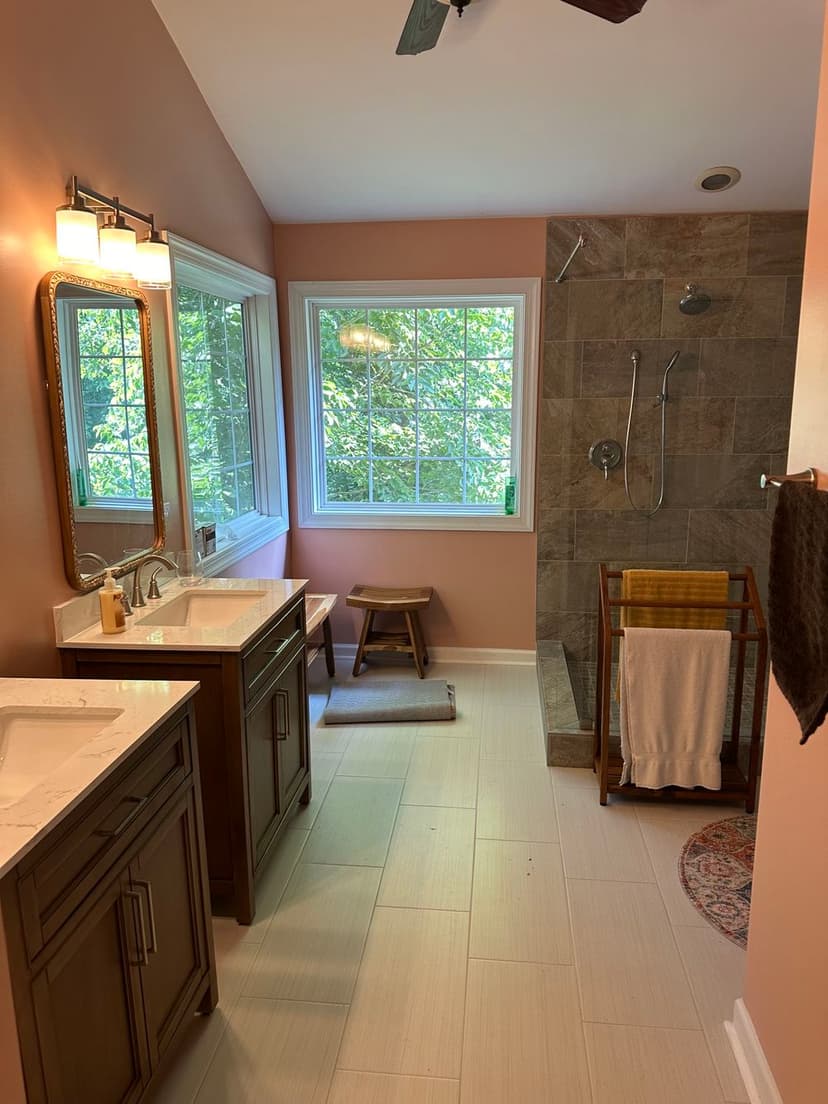 Modern bathroom with natural light, dual vanities, and a walk-in shower. Warm peach walls.