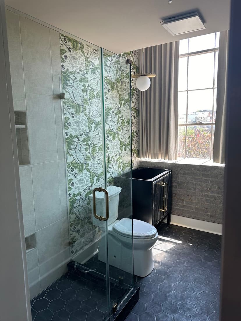 Modern bathroom design featuring glass shower, patterned wallpaper, and sleek black vanity.