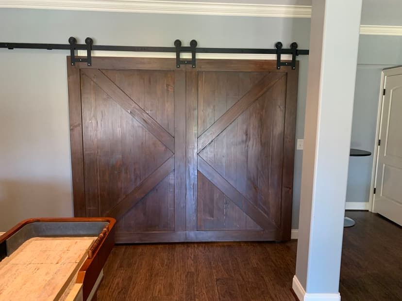 Wooden sliding barn door with x-pattern, mounted on a black rail in a modern interior.