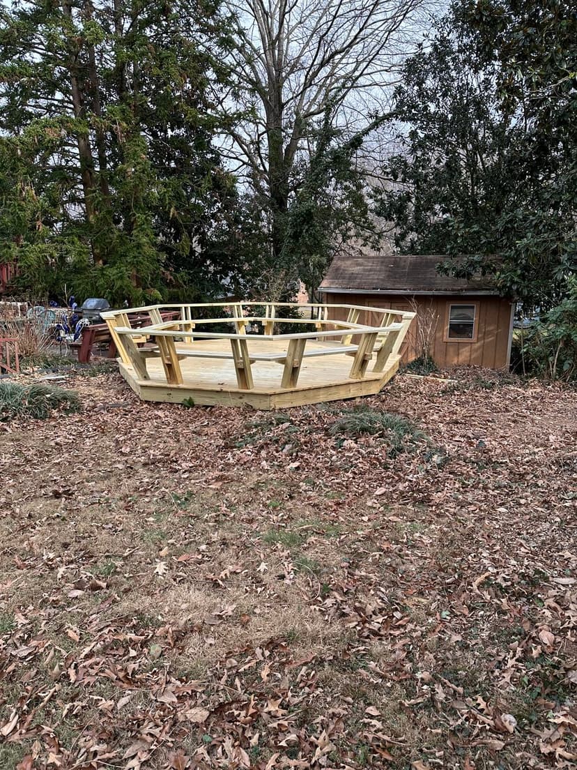 Wooden boat frame under construction in a leaf-covered yard near a shed.